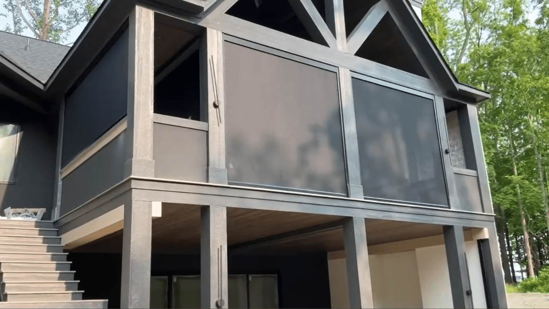 Two-story home with motorized retractable screens enclosing an elevated patio, surrounded by trees